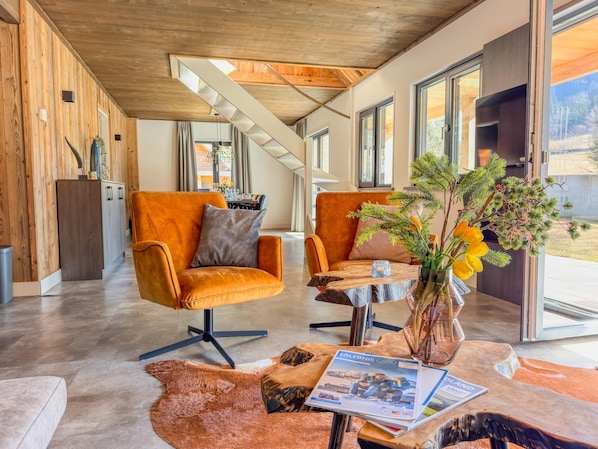 A modern interior with a wooden ceiling, two orange armchairs, a wooden coffee table, and a vase with flowers. - Premium chalet with sauna and terrace at a lake (Afritz am See)