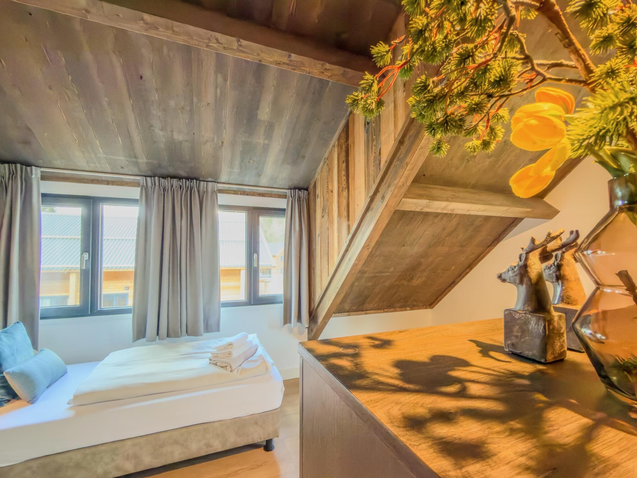 Ein Schlafzimmer mit einem Bett, einem Fenster, einer Holzbalkendecke und einer dekorativen Hirschskulptur.