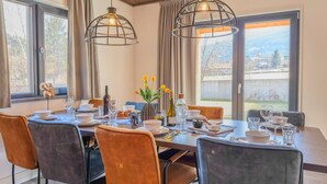Un espace repas avec une longue table dressée pour le repas, deux lampes suspendues et une vue sur l’extérieur.