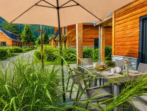 Eine Holz-Blockhütte mit einer Terrassentisch und -stühlen, umgeben von viel Grün und einem Bergpanorama.