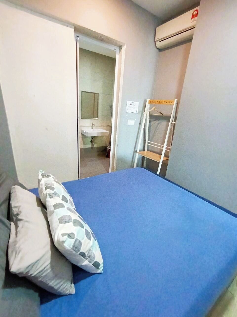 Quarto com colchão azul, travesseiro branco, prateleira branca e ar condicionado.