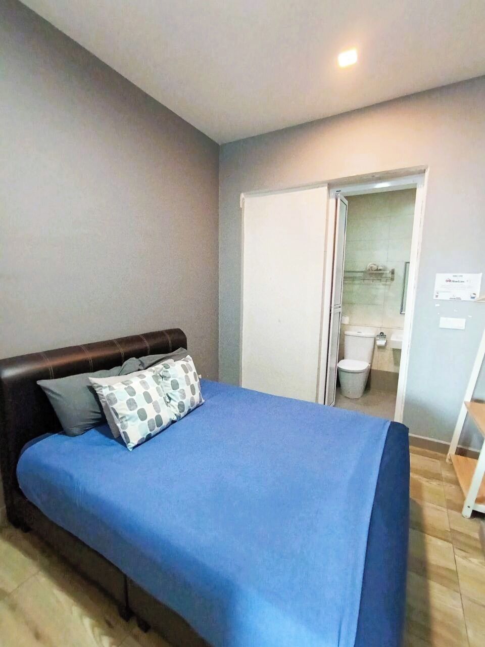 A bedroom with a bed, a nightstand, a closed door, and a bathroom visible through an open door.