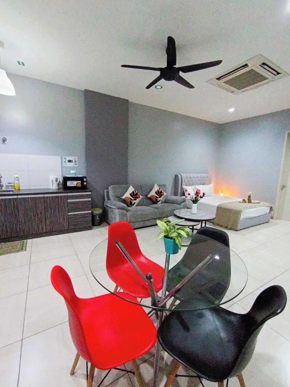 Una sala de estar moderna con un sofá, una mesa de comedor con sillas, un ventilador de techo y una zona de cocina con mostrador.