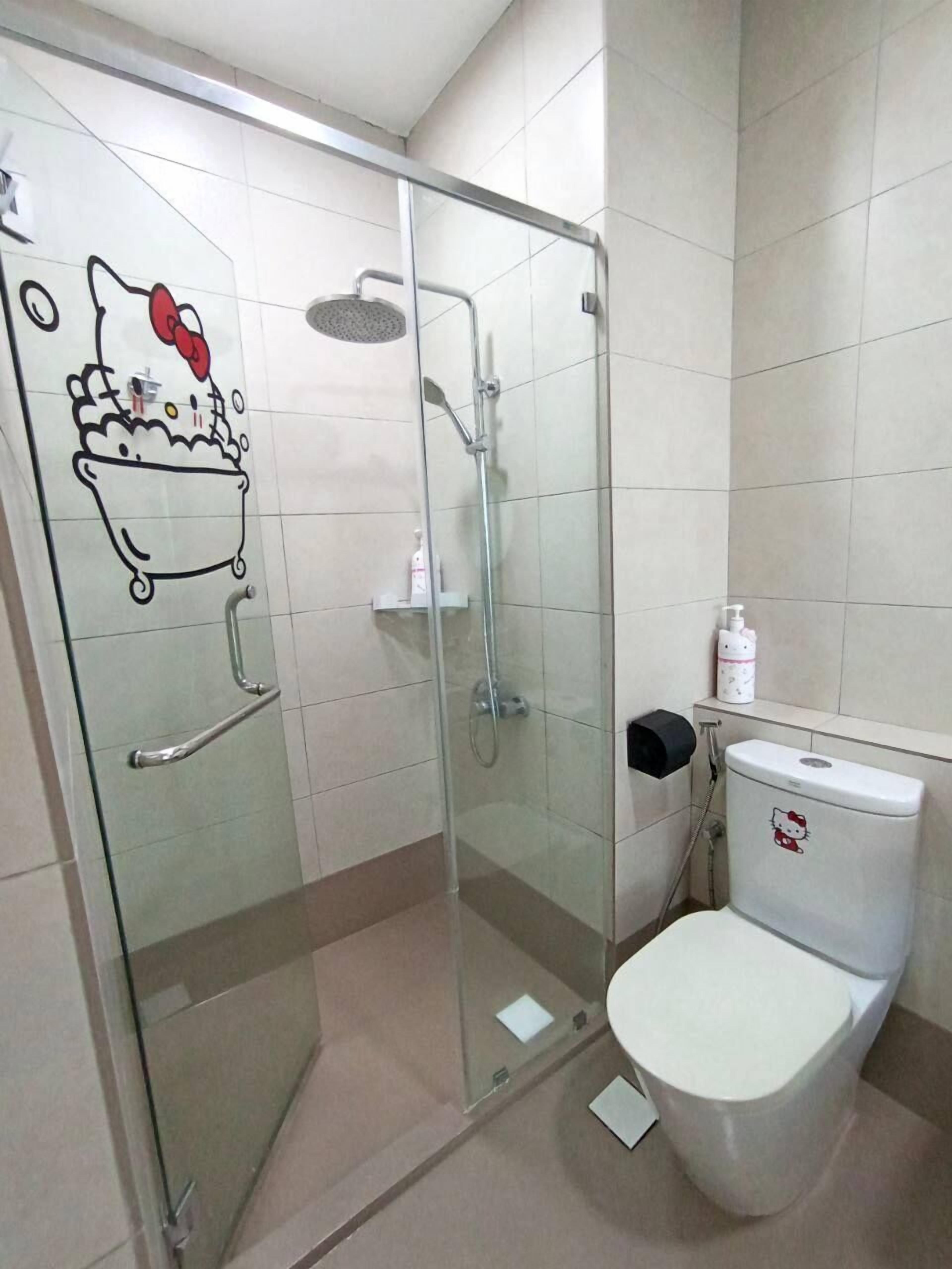 A bathroom with a glass-enclosed shower, a toilet with a Hello Kitty decal, and a handrail on the door.