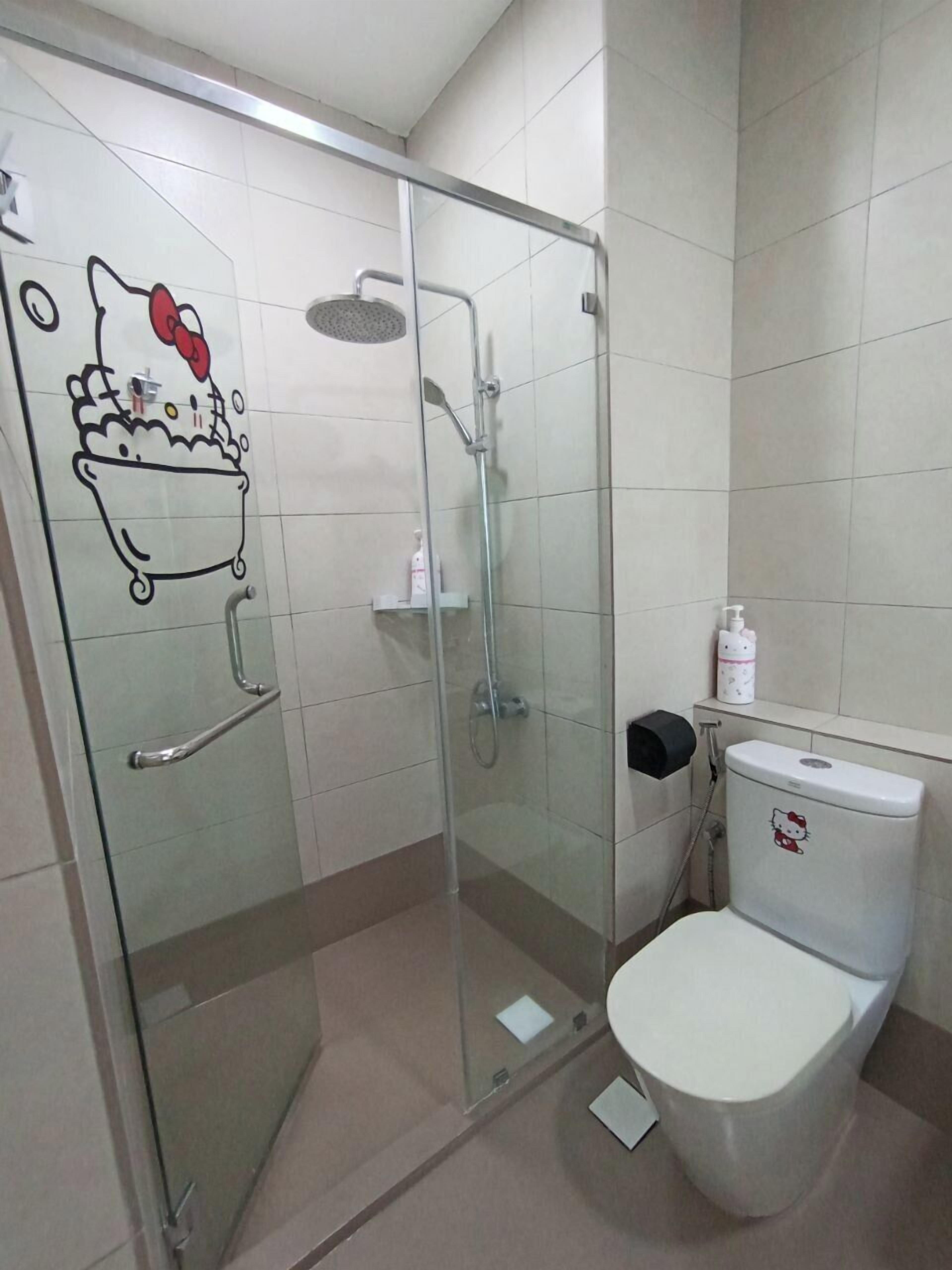 A bathroom with a glass shower enclosure, a toilet with a Hello Kitty design, and a handrail on the door.