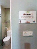 A bathroom with a toilet, a shower, and a wall-mounted sign instructing guests to switch off the water heater's switch after using it.