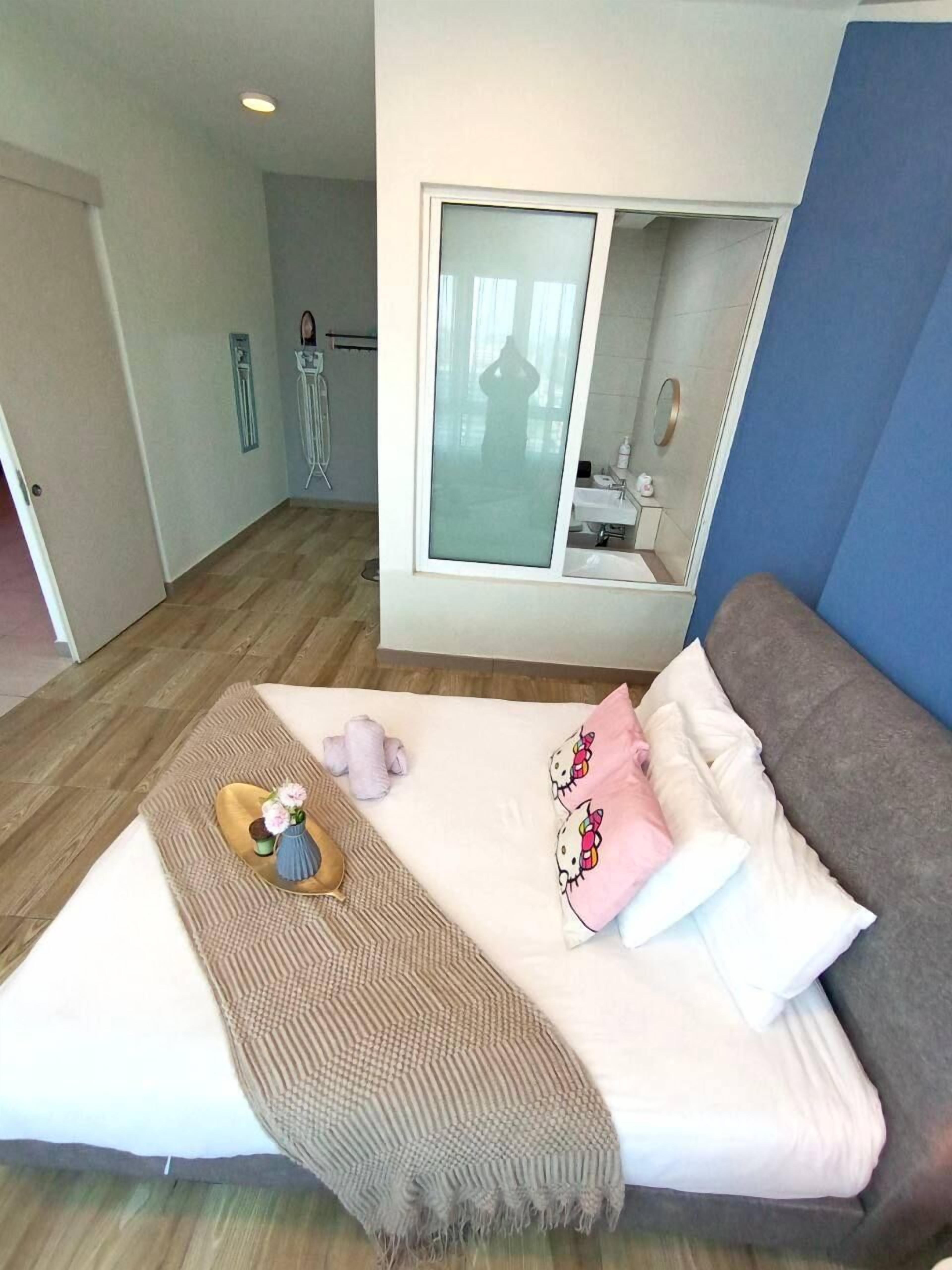 A bedroom with a bed, a window, a mirror, and a bathroom visible through the window.