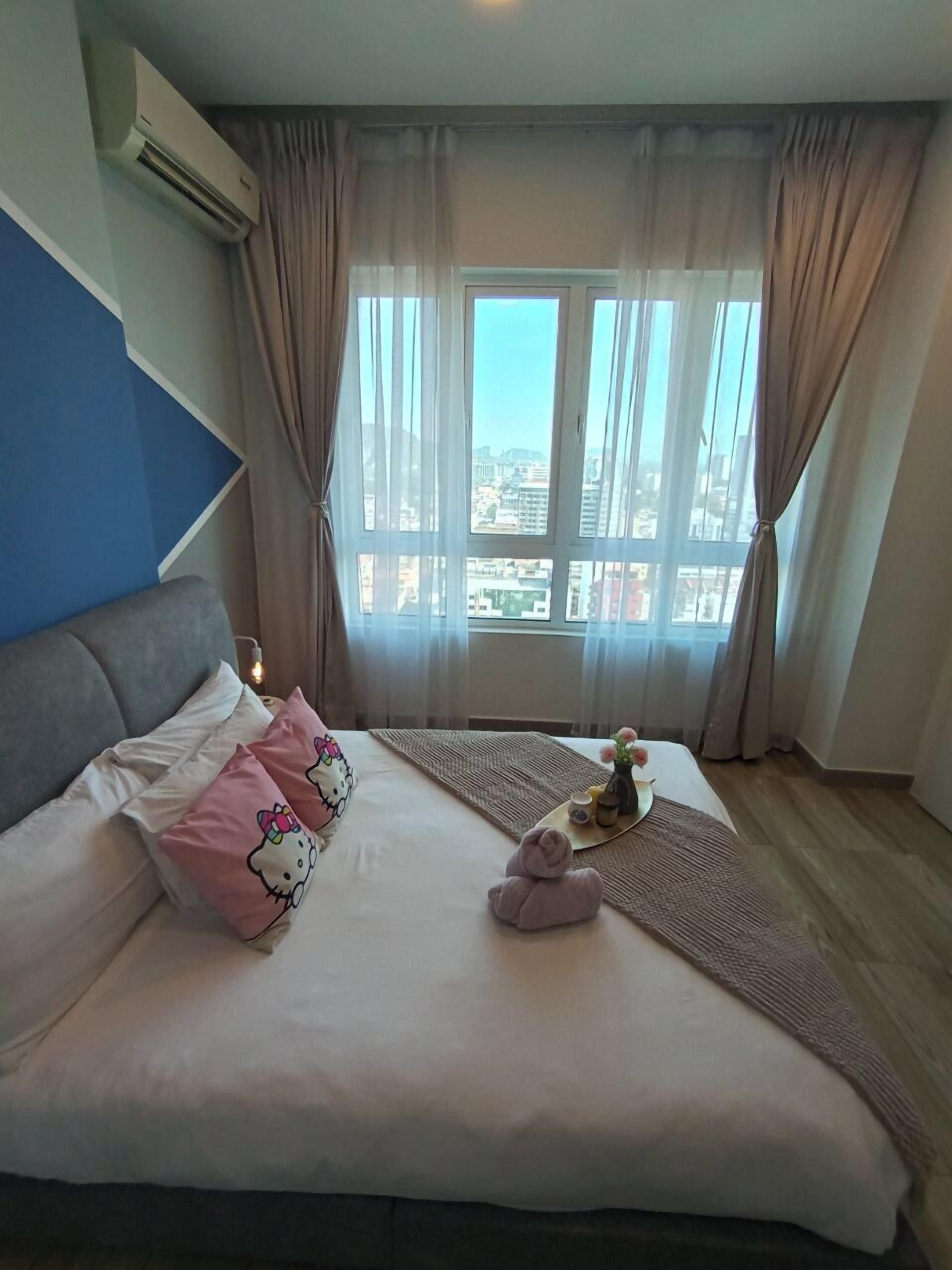 A hotel room with a bed, a view of the city, and an air conditioning unit.