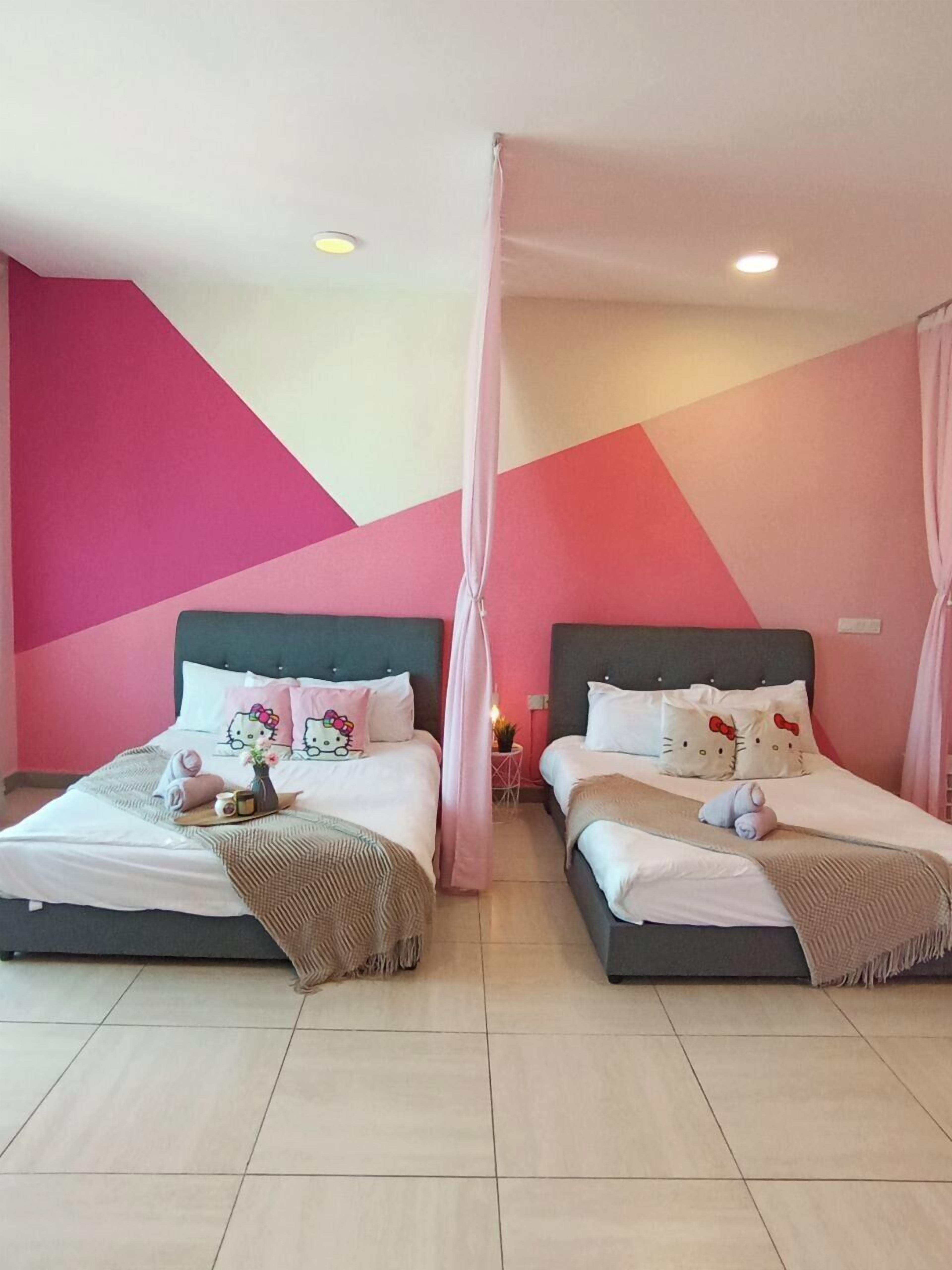 A hotel room with two beds, each with Hello Kitty pillows, a pink canopy, and a small table with a vase and a cup.