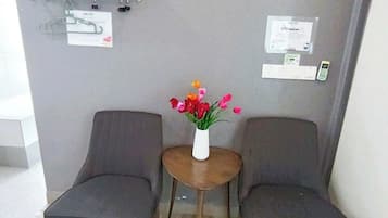 A room with two dark-colored chairs, a small round table with a vase of flowers, a towel rack with folded towels, and a wall-mounted phone.