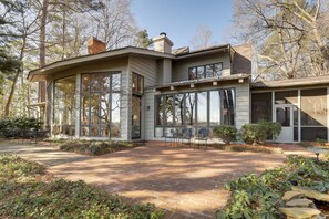 Ein modernes Haus mit großen Fenstern, einer Ziegelterrasse und Sitzgelegenheiten im Freien.