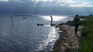 Une plage avec un ciel dégagé, une eau calme et une côte visible au loin.