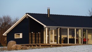 Une maison à l’extérieur sombre, dotée d’une grande cheminée et d’une véranda fermée par des vitres.