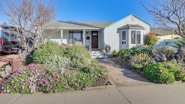 Einbungalow mit einer Veranda, einer Garage und einem gepflegten Garten mit verschiedenen Pflanzen und Blumen.