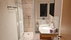 Un baño estrecho con ducha, lavabo y espejo.