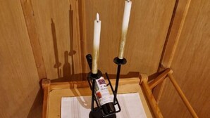 Una mesa de madera con dos velas sobre soportes, una botella y un pedazo de papel.