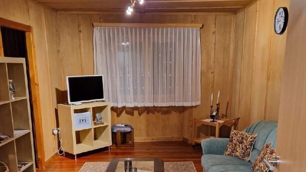 Una sala de estar acogedora con piso de madera, un sofá azul, una mesa de centro, un televisor sobre un mueble bajo y una estantería.