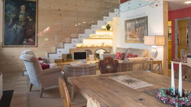 Ein modernes Wohnzimmer mit einer Holztreppe, einem Esstisch und einem großen Gemälde an der Wand.