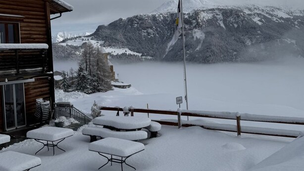 A wooden cabin with a snow-covered patio and a view of a mountain.