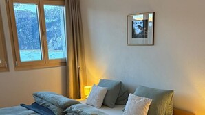 A bedroom with a wooden bed, two bedside lamps, a window with a view of mountains, and a framed picture on the wall.
