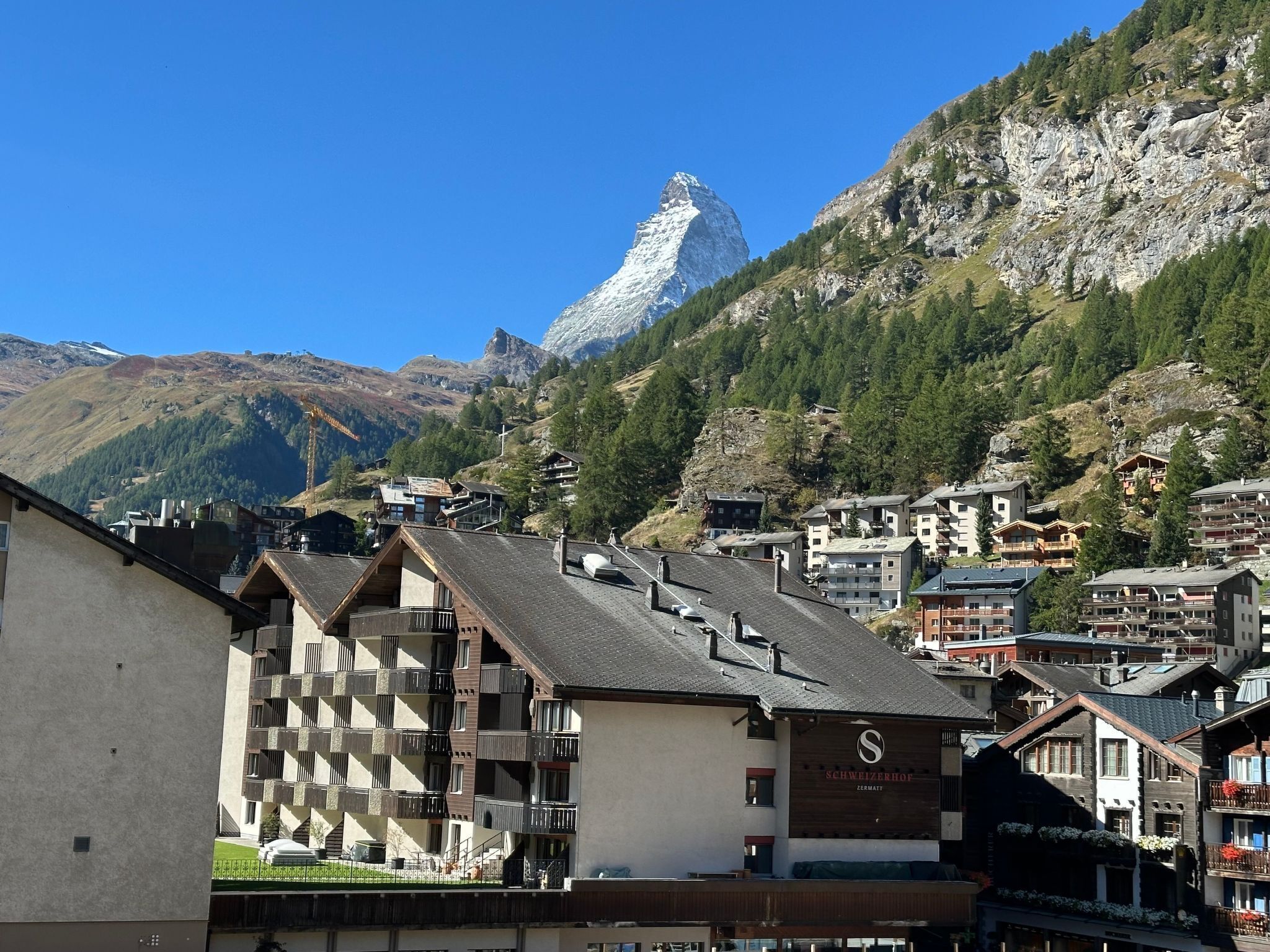 Une ville de montagne aux bâtiments de style chalet traditionnel, avec un sommet montagneux imposant en arrière-plan et un ciel bleu dégagé.