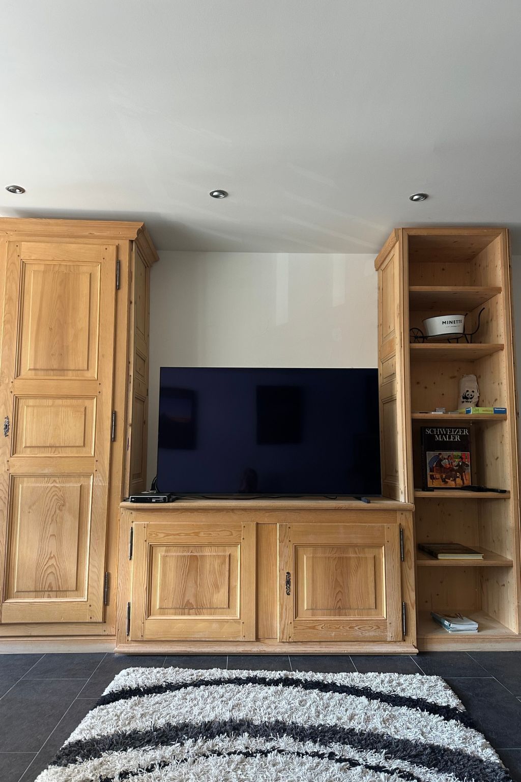 Een woonkamer met een grote flatscreen televisie, houten kasten en een vloerkleed.