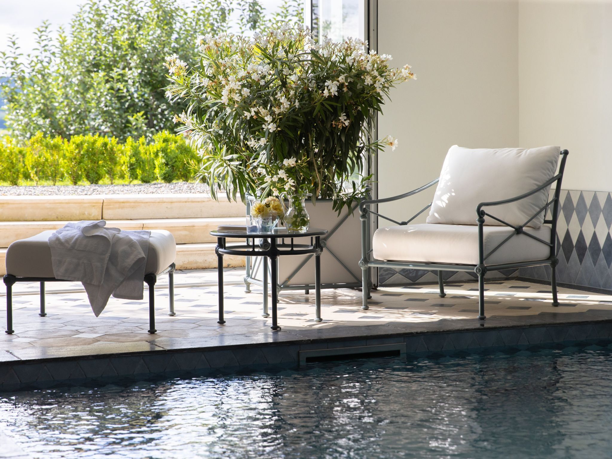 Un espace aménagé au bord de la piscine, avec une chaise et une petite table, un banc couvert et un pot de fleurs.