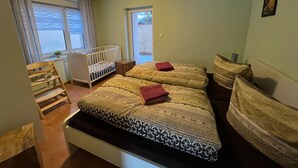 Un dormitorio con dos camas, una cuna, una silla de madera y una ventana con cortinas.