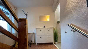 Un pasillo con escaleras de madera, un armario blanco, un radiador y una planta en maceta.