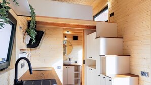 Una cocina moderna con pisos y gabinetes de madera, un lavamanos negro y una planta colgante.