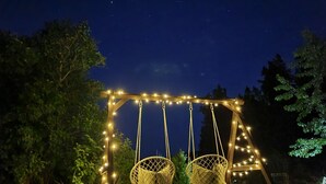 Un columpio con luces de cuerda y dos sillas de mimbre bajo un cielo estrellado.