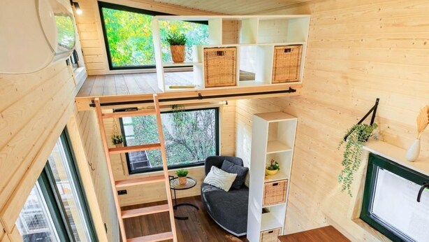 Un interior moderno y funcional con un entrepiso para dormir, una pequeña cocina y una zona de estar con vistas a espacios verdes.
