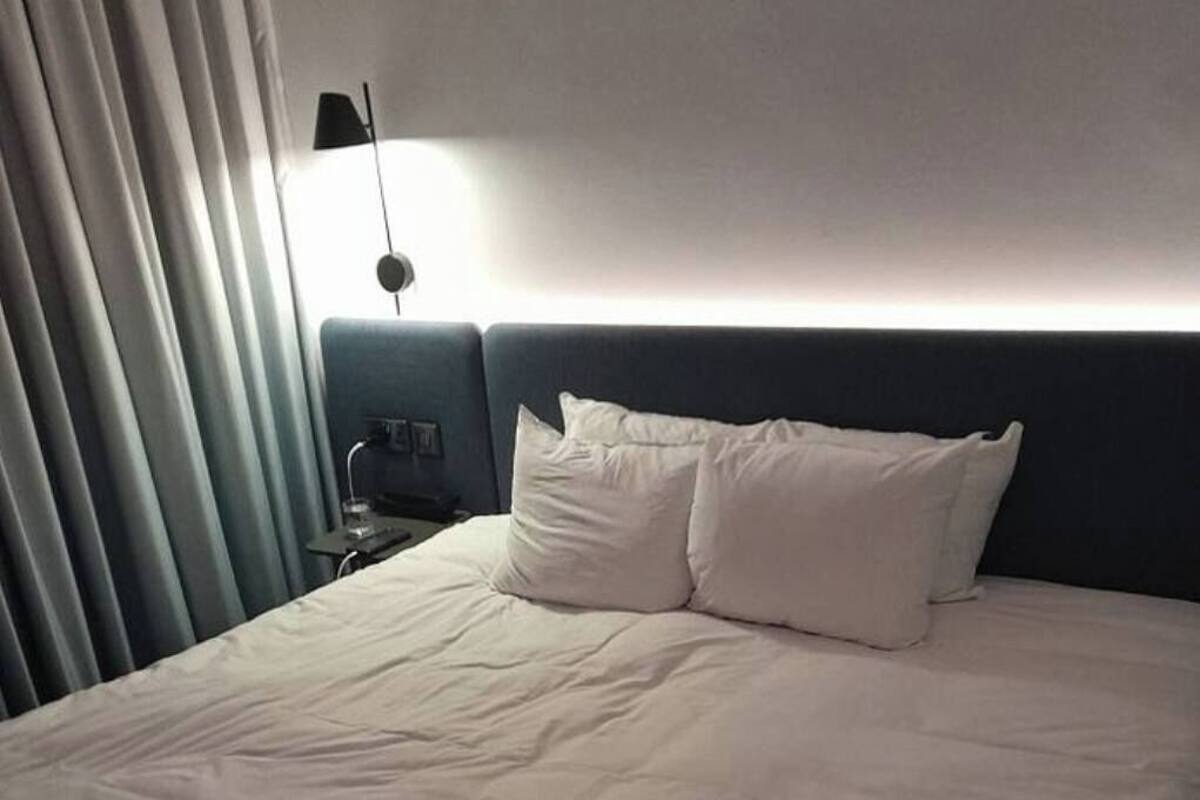 Ein Hotelzimmer mit einem großen Bett, einem Nachttisch, einer Lampe und Blick ins Freie.