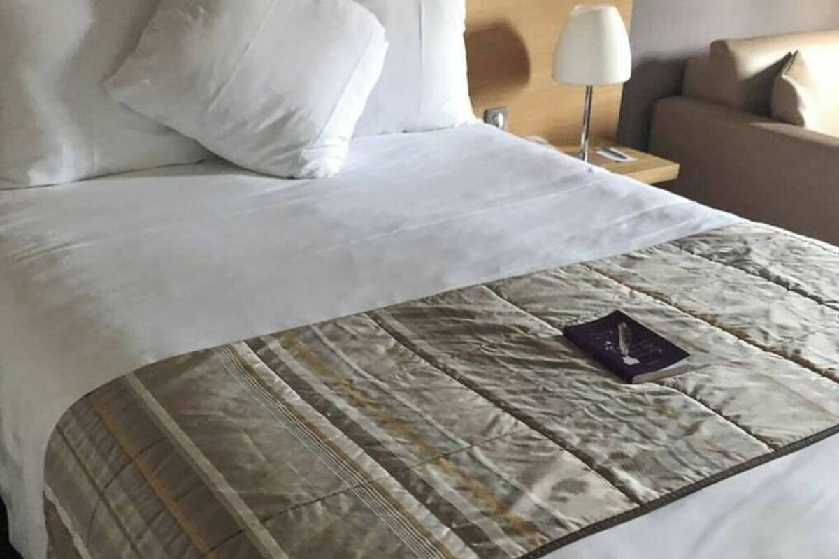 Ein ordentlich bezogenes Bett mit weißen Laken und einer gemusterten Tagesdecke, eine Nachttischlampe und ein Sofa mit Kissen.