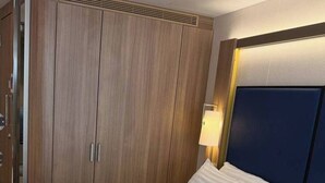 Een hotelkamer met een groot bed, een houten garderobe en een nachtkastje met een lamp.