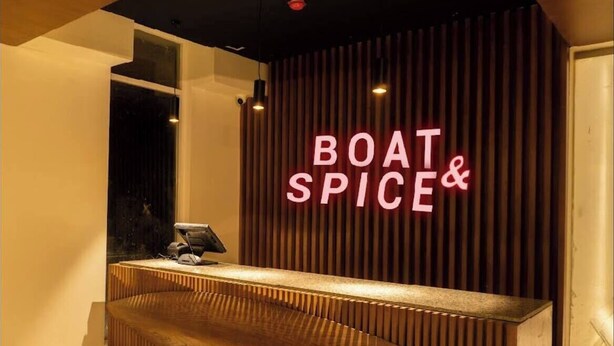 Een houten receptiebalie met een neonbord waarop 'BOAT & SPICE' staat.
