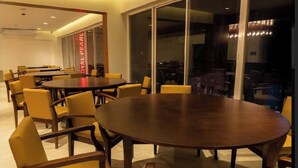 Een vergaderzaal met een grote ovale tafel, omringd door gele stoelen, grote ramen en een zichtbare airconditioning.