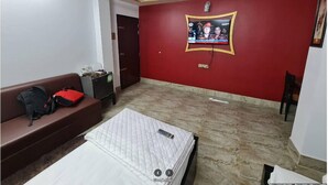Een kamer met een rode wand, een televisie die eraan bevestigd is, een bank, een bed met matras en een plafondventilator.
