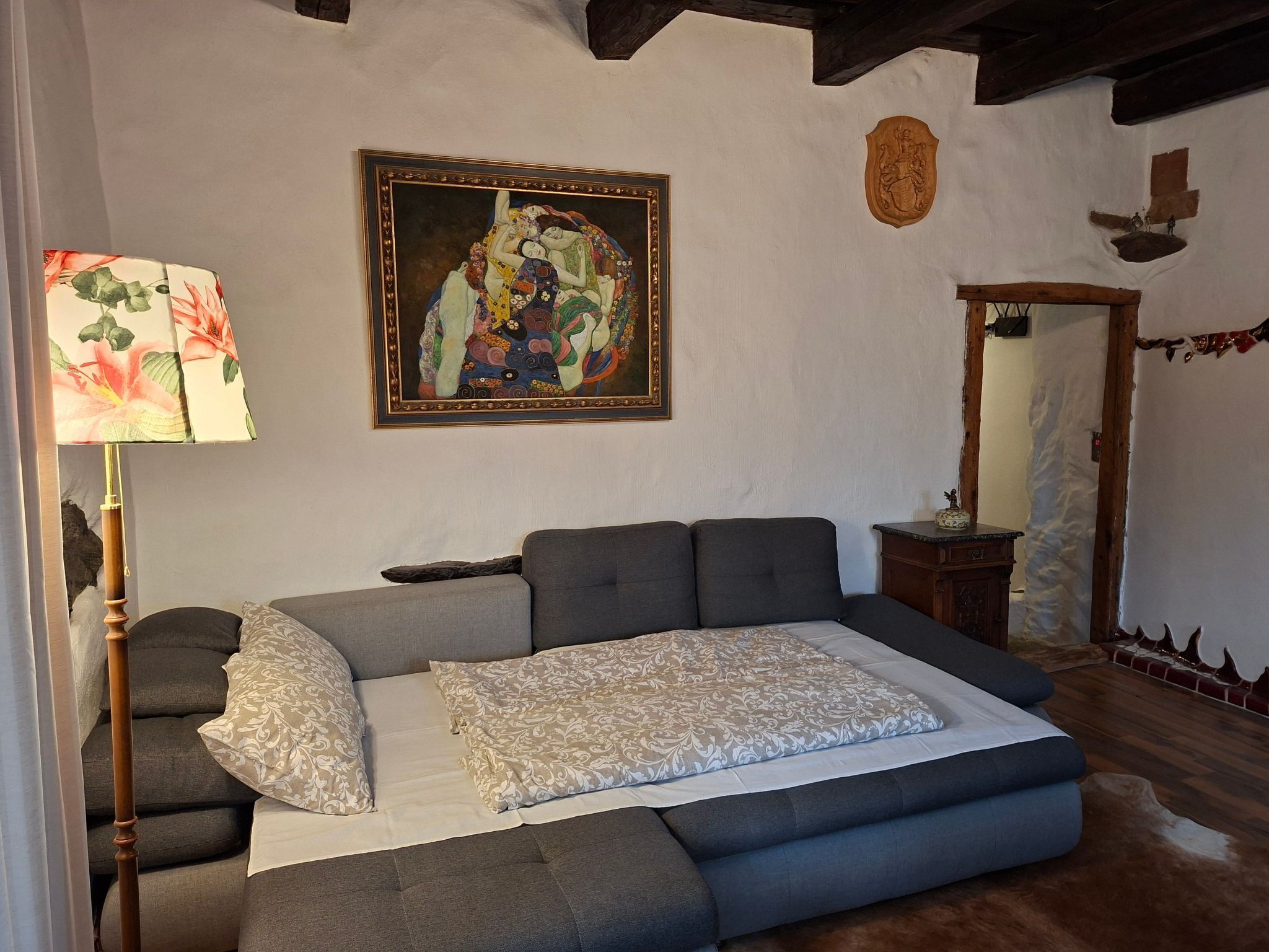A bedroom with a sofa bed, a wooden floor, a painting on the wall, and a mirror.
