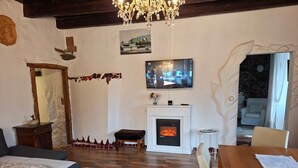 A cozy living room with a fireplace, a television mounted on the wall, and a dining area with a table and chairs. - ApartmentDonaustrand by Interhome (Leiben)