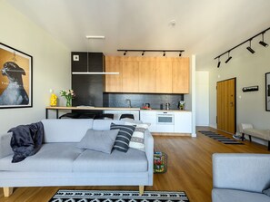 A modern living room with a grey sofa, a wooden dining table, and a kitchen with wooden cabinets and a black refrigerator. - Suite mit Balkon by Interhome (Łódź)