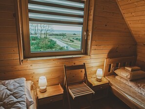 Ein gemütliches Cabin-Zimmer mit Holzvertäfelung, einem Fenster mit Blick auf eine Straße und Bäume, einem Bett, einem Sessel und zwei Nachttischen mit Lampen.