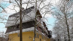 Een meerlaags gebouw met een gele gevel, omgeven door met sneeuw bedekte bomen en een besneeuwd pad.