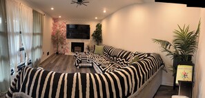 A modern living room with a sectional sofa, a fireplace, and a flat-screen TV mounted on a brick wall. - Spacious Home Airport 10 Min (East Point)