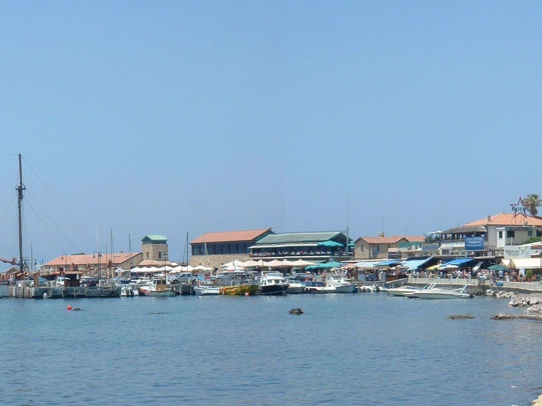 A marina with boats docked, a lighthouse, and buildings with red roofs.
