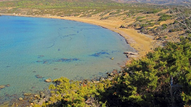 Un paisaje costero con aguas azules cristalinas, playa de arena y colinas verdes al fondo.