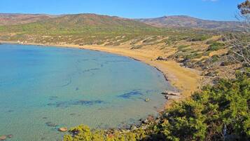 A coastal landscape with clear blue waters, sandy beach, and green hills in the background.