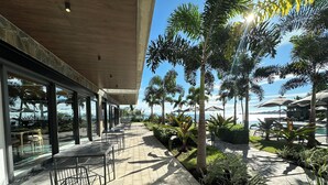 Un espace extérieur aménagé en terrasse, avec des tables et des chaises, entouré de verdure et offrant une vue sur une piscine et l’océan.