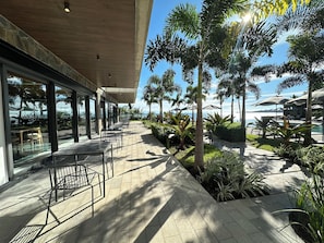 Eine Außenpatio-Terrasse mit Tischen und Stühlen, umgeben von Grünpflanzen und mit Blick auf einen Pool und den Ozean.
