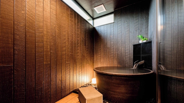 A modern bathroom with wooden paneling, a large bathtub, and a small plant. - Hakone Mori No Sato (Hakone)